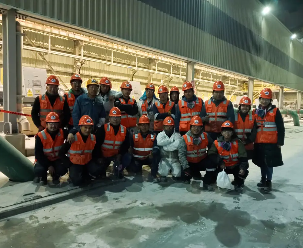 Un grupo grande de trabajadores con cascos y chalecos naranjas posando en una fábrica.